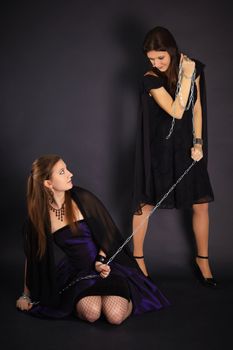 Two young girls playing master and slave on dark background