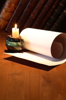 Old paper near lighting candle and stack of vintage books on wooden surface