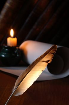 Closeup of quill pen standing on dark background with lighting candle and scroll