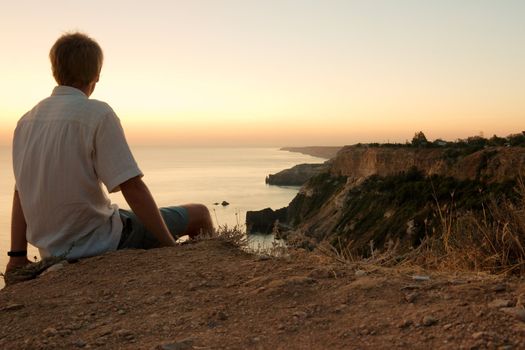 Man sitting on the edge of a cliff, staring at a majestic coastline