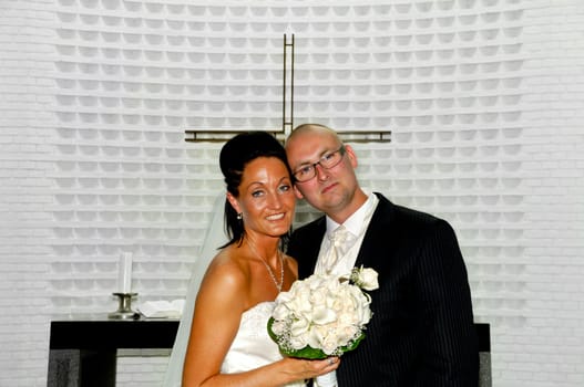 Happy bride and groom is standing together in front of cross