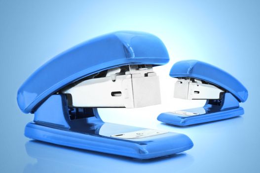 Close up of two blue office staplers isolated over blue light effect