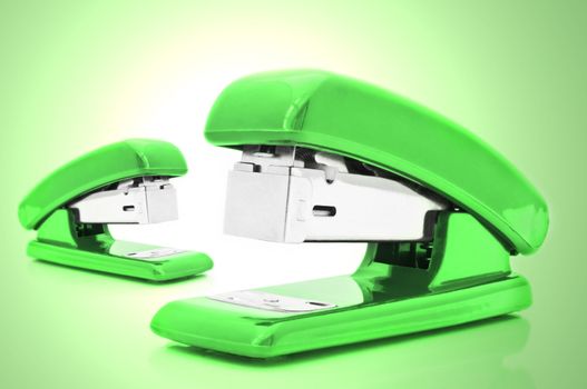 Close up of two green office staplers isolated over pale green light effect