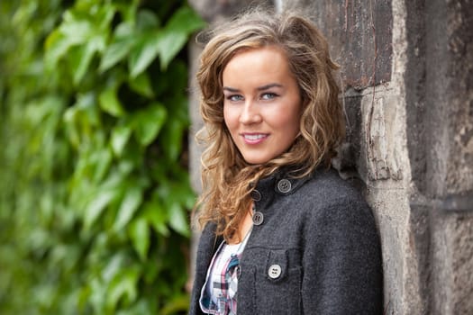 Portrait of young casual woman leaning against stone wall