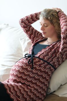 Young prengnant woman sitting an watching her abdomen.