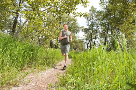 Handsome man in sportswear running in the forest