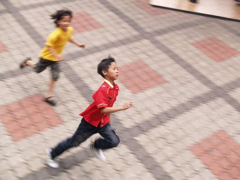 Two boys running trying to catch each other.