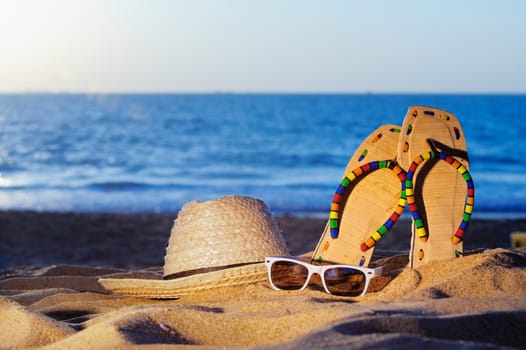 Wicker hat, sandal and glasses on the sandy beach