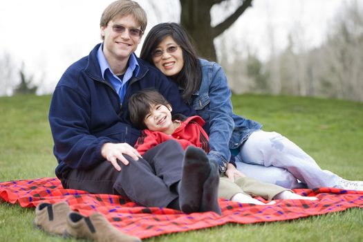 Father and mother sitting at park with disabled son, interracial family