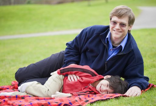 Father lying on blanket with disabled son at park