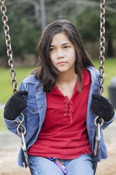 Angry, sad preteen girl sitting on swing