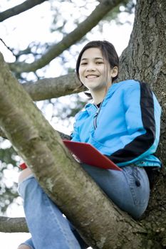 Preteen girl sitting in tree writing in journal or notebook