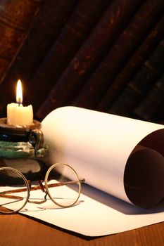 Scroll and old spectacles near lighting candle on dark background with vintage books