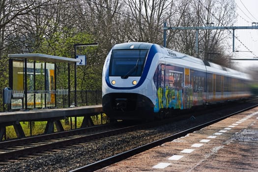 Suburb train passing by at small station on day in early spring