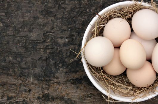 A bowl of freshly laid organic white eggs, set in a white ceramic bowl with straw. Set on an isolated wooden background. Set on a landscape format with copy space available.