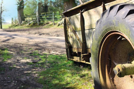 An old farm trailer in a country lane setting. Detail on the rusty tyre of the trailer set to right of image, with a countryside background. Set on a landscape format. Located in The New Forest area, Hampshire UK.