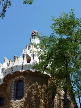 White roof of a house made of colored mosaic next to a tree at Park Guell, Barcelona, Spain
