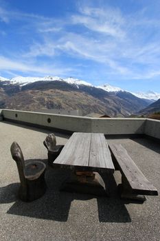 Wood bench, chairs and table on a terrace with view on beautiful snowy mountains by beautiful day