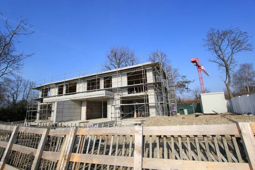 Residential house under construction next to a crane and behind a wood fence by beautiful weather