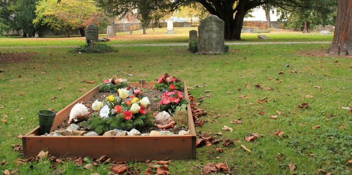 Tomb covered with colored flowers with autumn colored red leaves in a cemetery