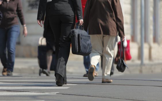 Image of a businesswoman's lower body. She is carrying a computer bag while crossing the street in a city.