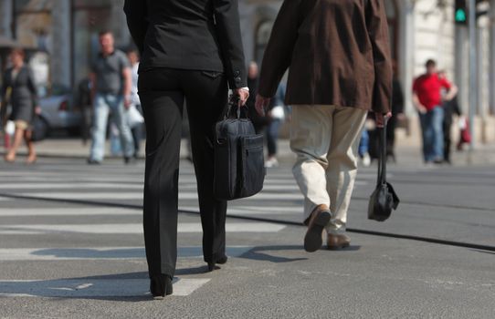 Image of a businesswoman's lower body. She is carrying a computer bag while crossing the street in a city.