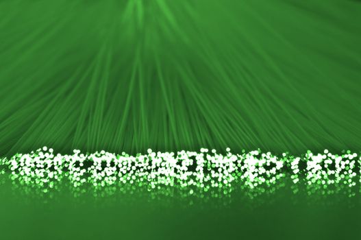 Close up on the ends of many illuminated green fiber optic strands which are reflecting into the green foreground
