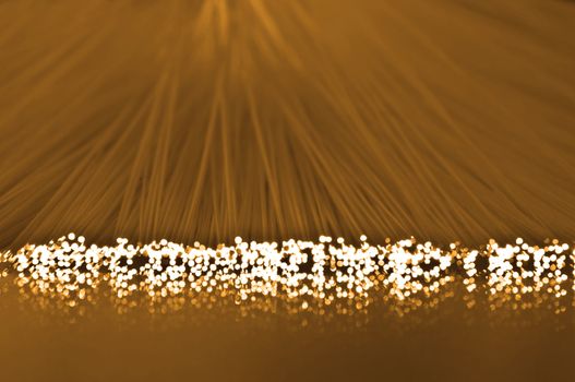 Close up on the ends of many illuminated fibre optic strands which are reflecting into the golden foreground