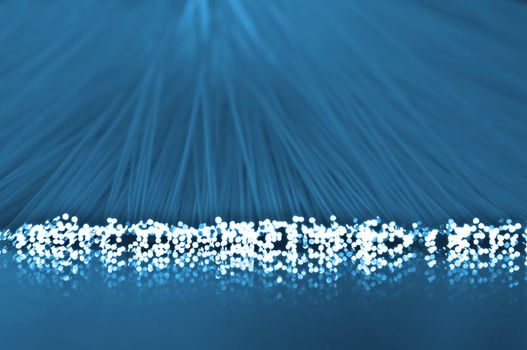 Close up on the ends of many illuminated blue fiber optic strands which are also reflecting into the blue foreground