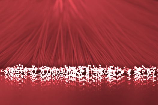 Close up on the ends of many illuminated fiber optic light strands which are reflecting into the red foreground