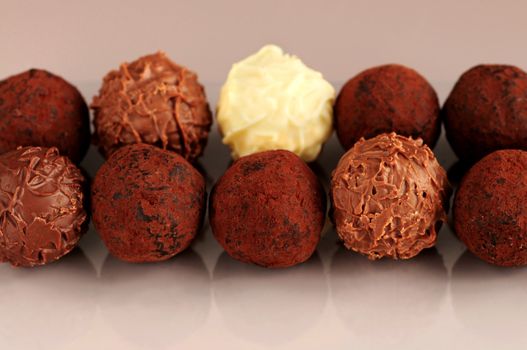 Several assorted chocolate truffles in rows on brown background