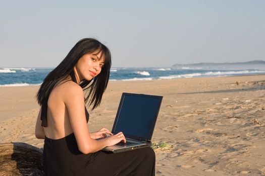 Attractive woman working on a laptop with the beach as background