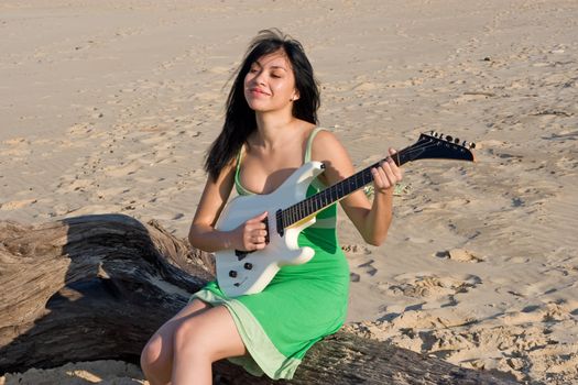 Girl in green dress playing a guitar at the beach