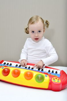 little girl sitting on the bed and plays on a children's keyboard