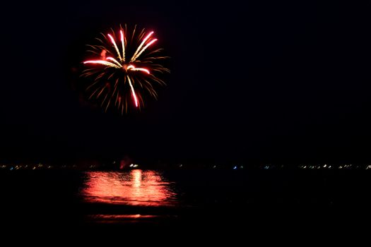 Beautiful fireworks going off over the dark night sky reflecting over the water.