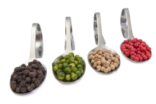 Four kinds of peppercorns in spoons isolated on white background