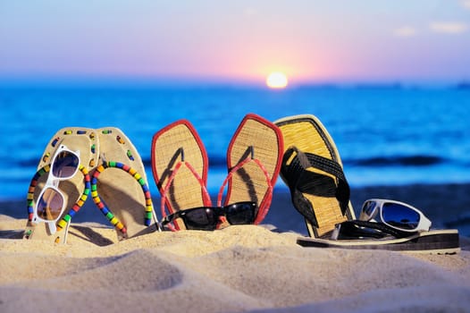 Three pair of beach sandals and glasses on the sandy beach