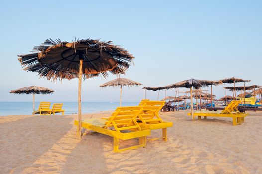Exotic beach umbrellas and deck-chairs on tropical coast