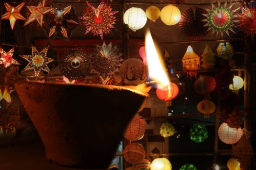 A traditional oil lamp lit in front of beautiful arrangement of sky lanterns, during the festive occassion of Diwali in India.