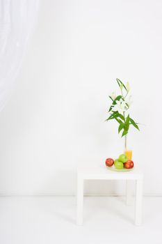 apples, a glass of juice and lilies on the table in a bright room