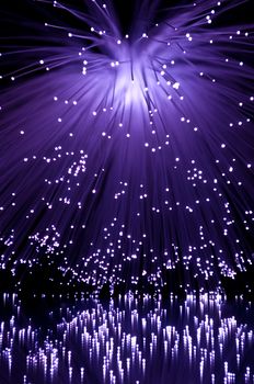 Many illuminated violet fiber optic light strands cascading down and reflecting into the foreground. Black background