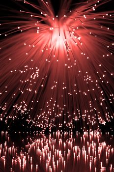 Many illuminated red fiber optic light strands cascading down and reflecting into the foreground. Black background