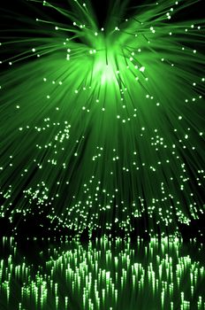 Many illuminated green fiber optic light strands cascading down and reflecting into the foreground. Black background