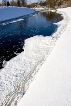 Fragment of the river in winter and ice passing pieces and rural houses on the hill.