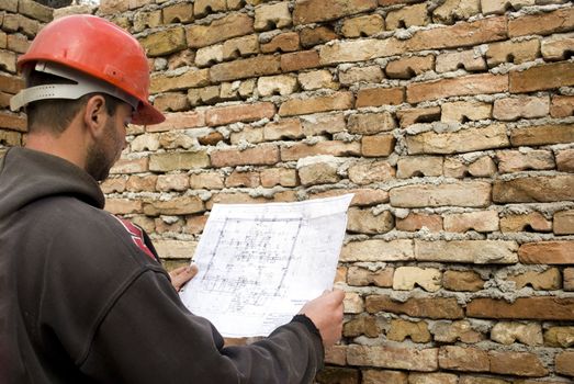 young male builder holding engineer project in front of brick wall