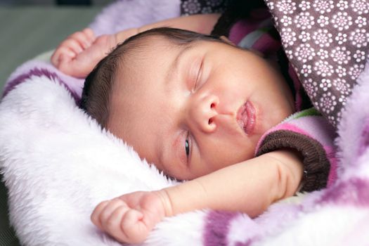 A newborn baby girl waking up from sleep and stretching under blankets.