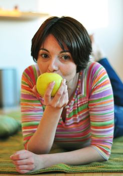 Portrait of happy young woman eating an apple on floor at home
