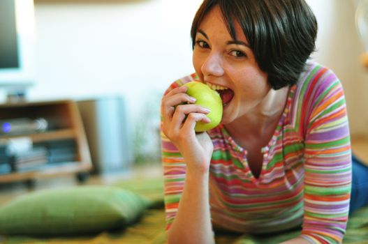 Portrait of happy young woman eating an apple on floor at home