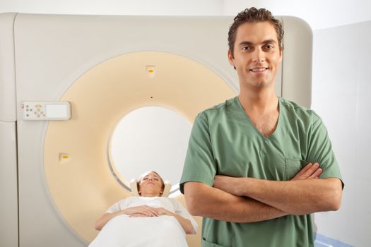 A CT scanner technician standing infront of a CT Scanner with a patient