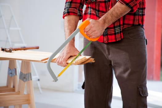 A detail of a man cutting wood with a small hand saw